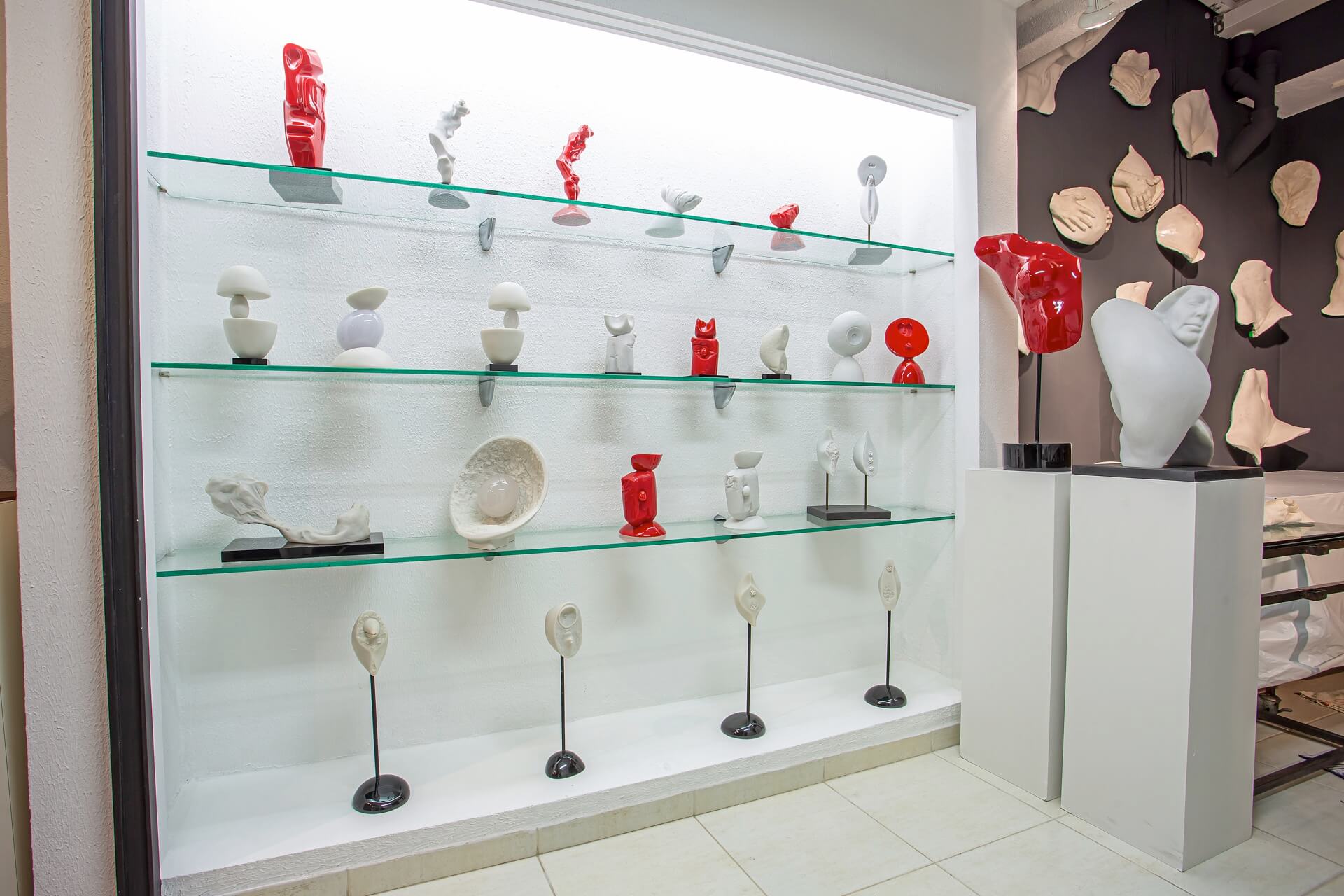 Vitrine do ateliê com coleção de esculturas em mármore e resina vermelha sobre prateleiras de vidro